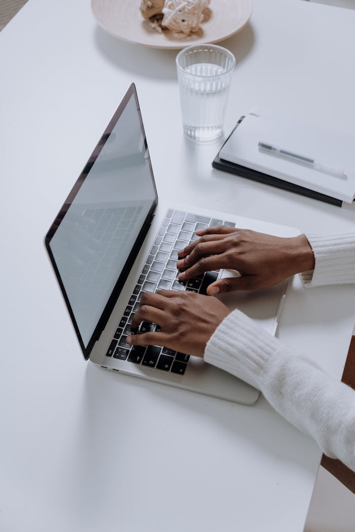 embark A woman typing on a laptop at a minimalist, modern home office desk, showcasing productivity.